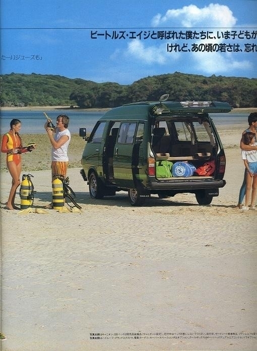 A photo of a green HiAce on a beach with its hatch open. It’s full of adventure gear. Two people stand nearby, prepping for a scuba dive. Their tanks are on the ground.