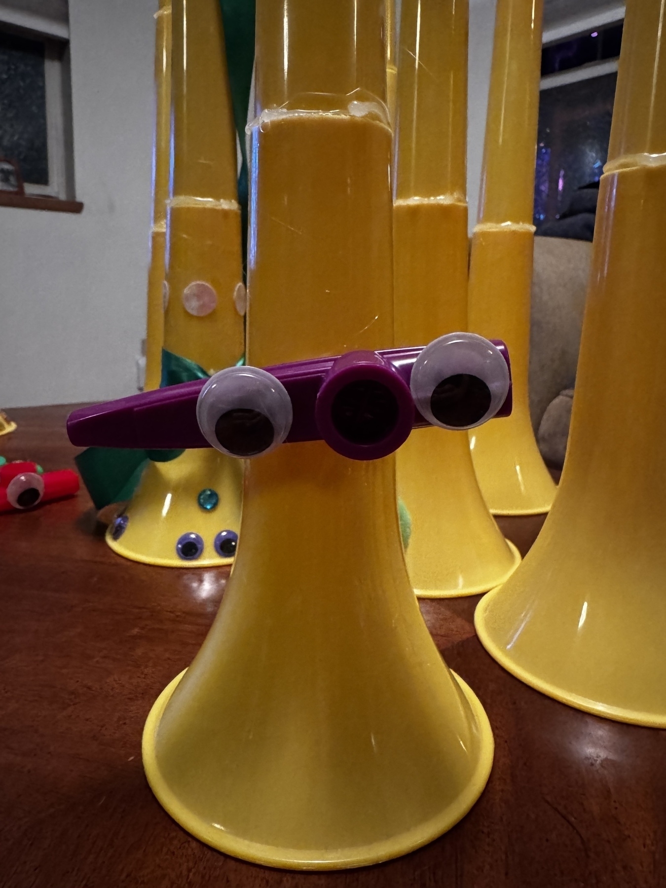 A photo of a kazoo hot glued to a vuvuzela but now with two googly eyes glued to the kazoo. 